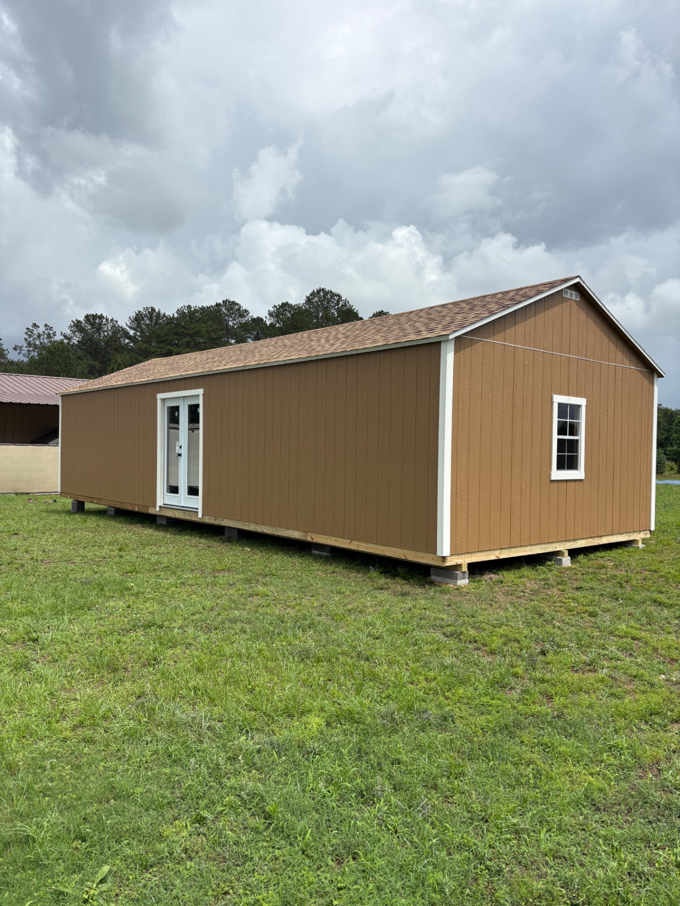 Long brown shed with white trim, a white glass-panel double door on the side and a grid window on the gable end