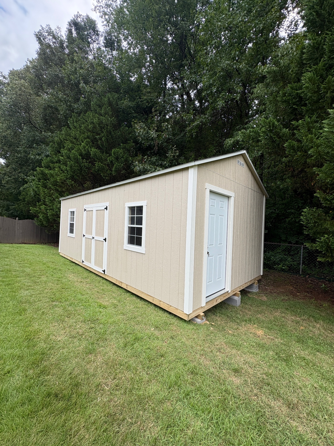 Long tan shed with a white house door on the gable end and double doors between two grid windows on the side