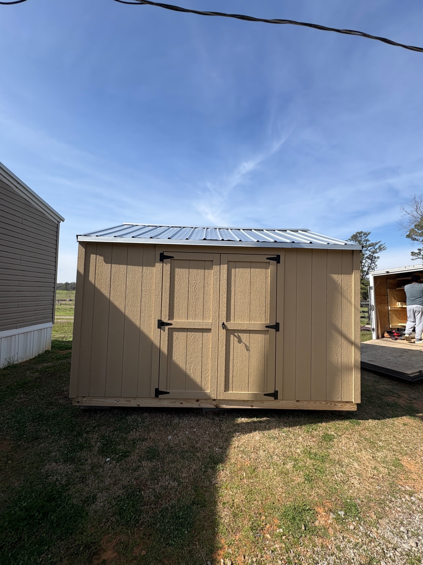 Tan shed with matching double doors, black hardware and a light-colored ribbed metal roof