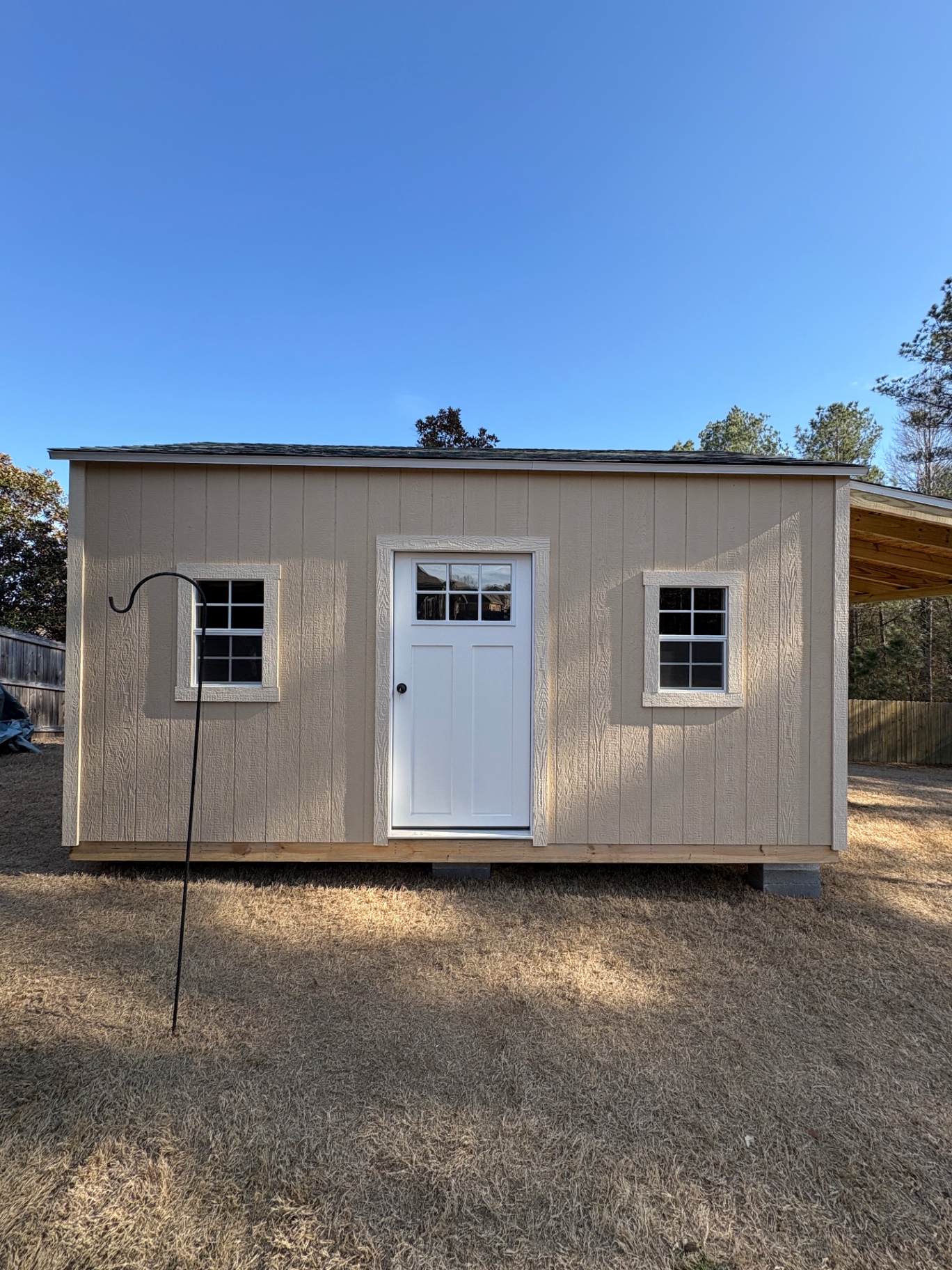 Tan shed with a white craftsman-style door with a divided glass panel and a grid window on each side