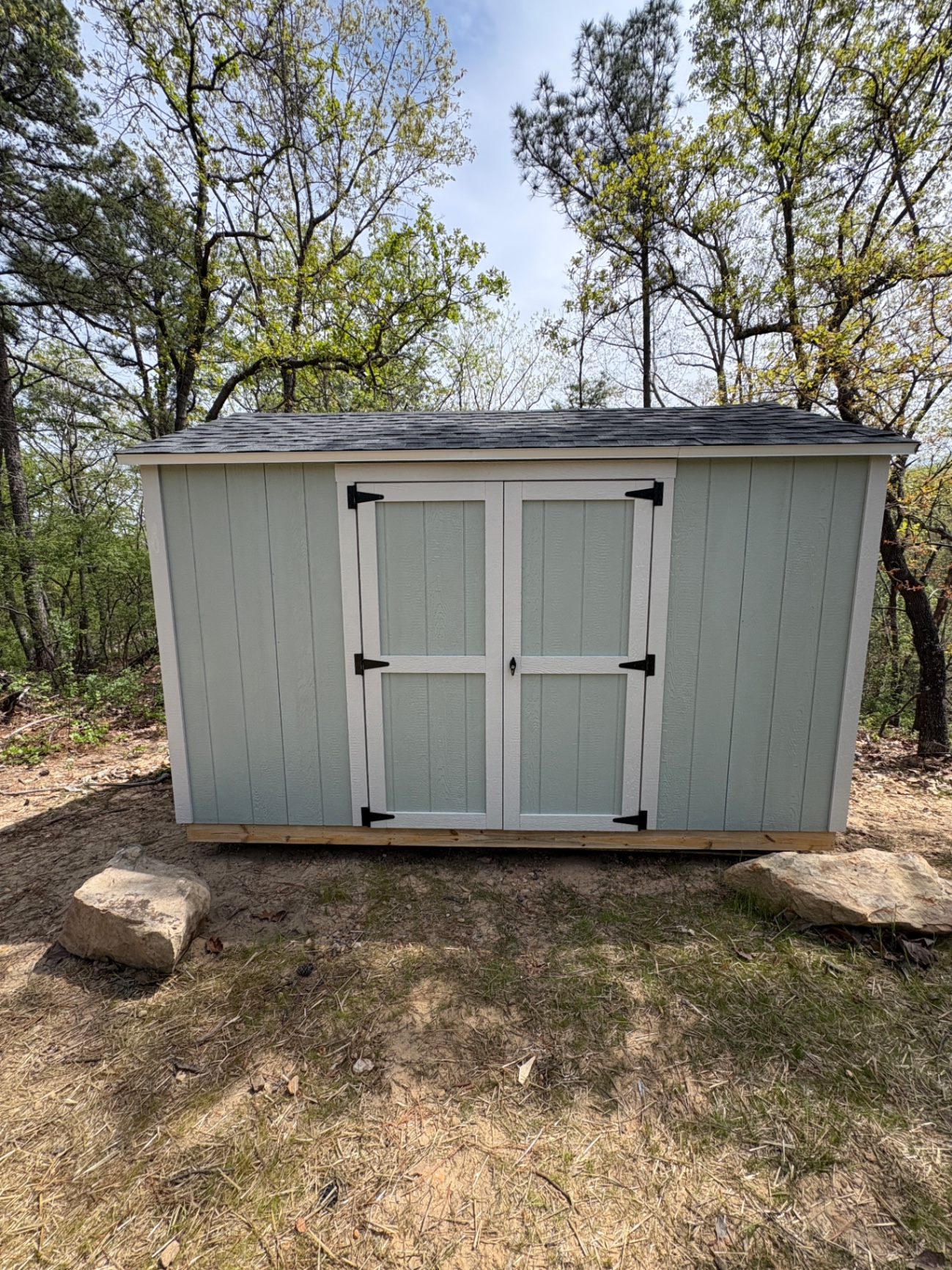 Light seafoam shed with white trim and double doors, set on a cleared spot in the woods