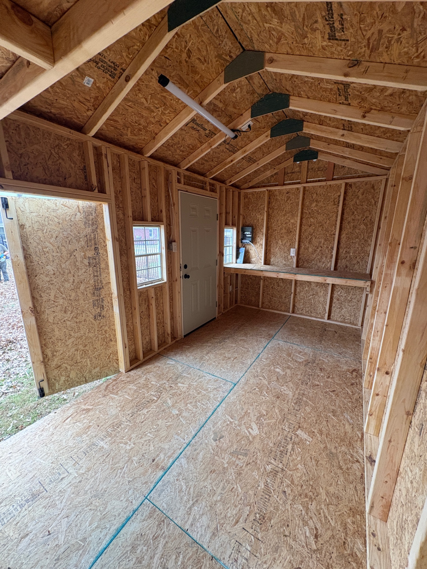 Inside a shed with a workbench along the wall, an outlet, a house door, two windows and an open double-door bay