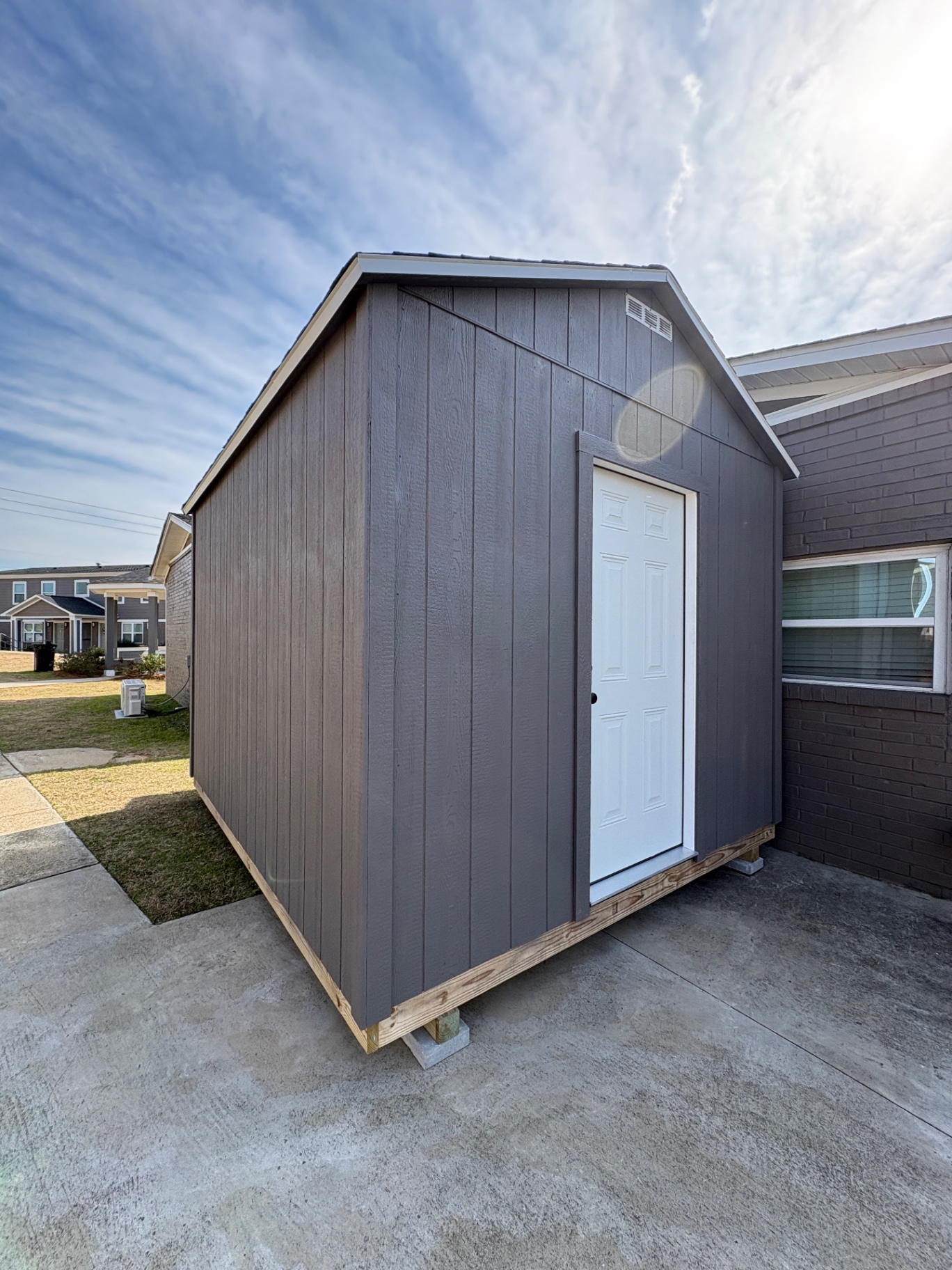 Corner view of a charcoal shed with a white six-panel house door, white roof trim and a gable vent, built on a concrete pad