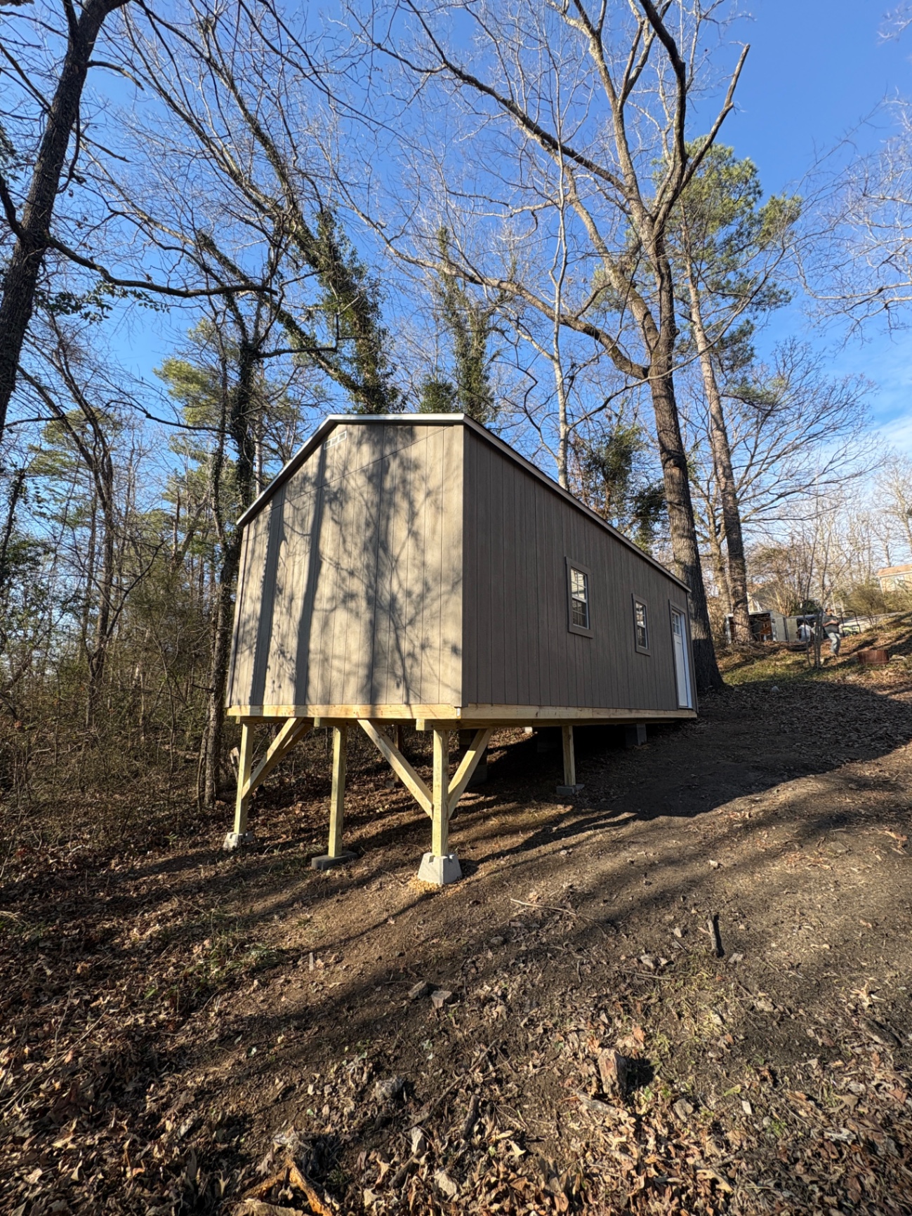 Angled view of a taupe shed standing on tall treated posts on a hillside in the woods