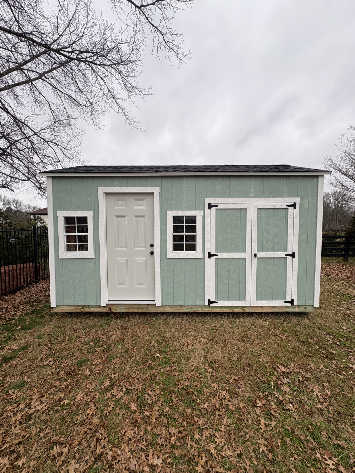 Mint green shed with a white six-panel house door, two grid windows and double doors on the long wall