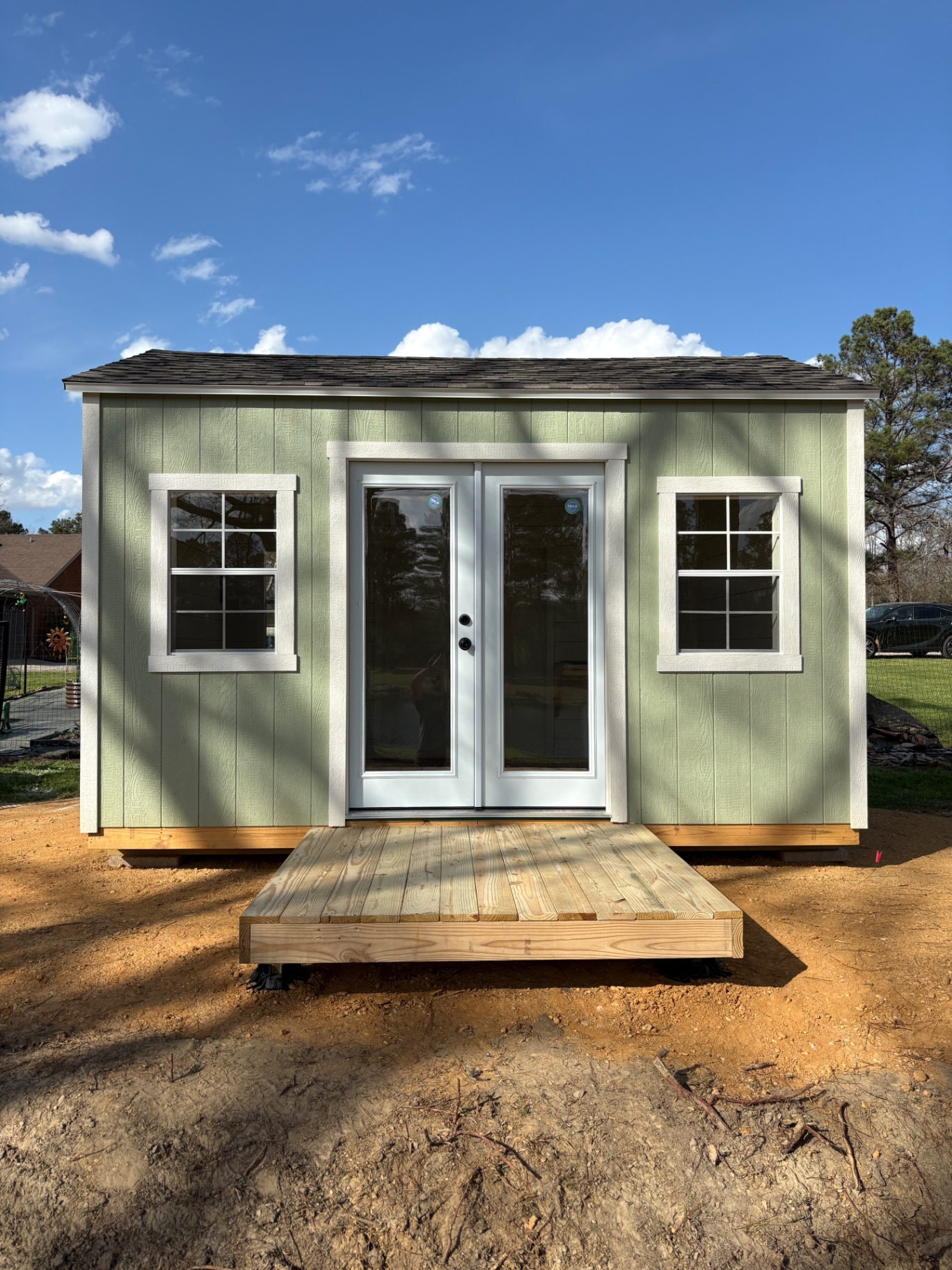 Sage green shed with white French doors, a grid window on each side and a low wood platform at the entrance