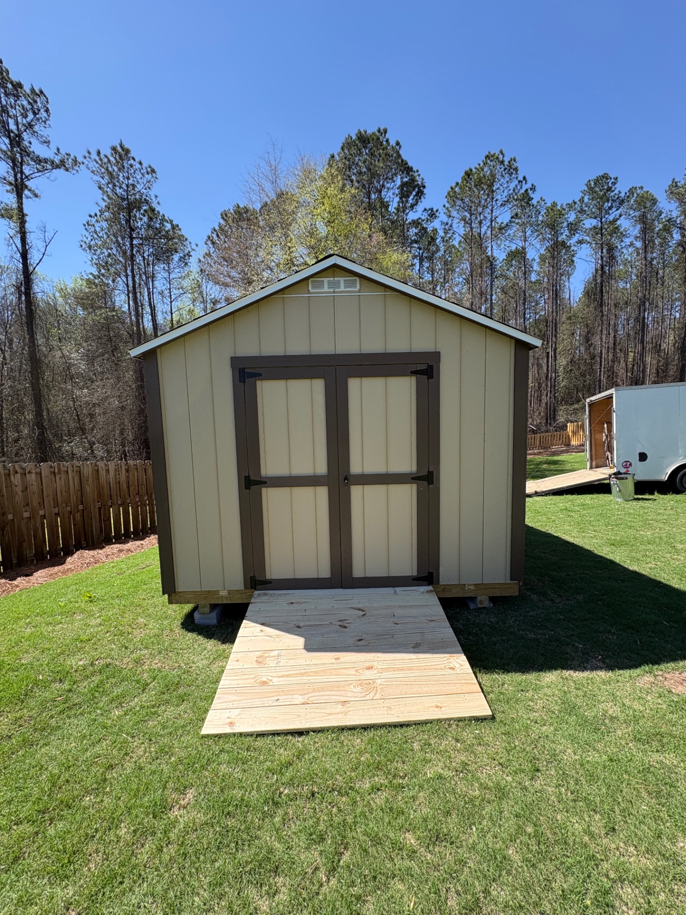 Tan shed with dark-trimmed double doors, a gable vent and a treated wood ramp built to fit the doors