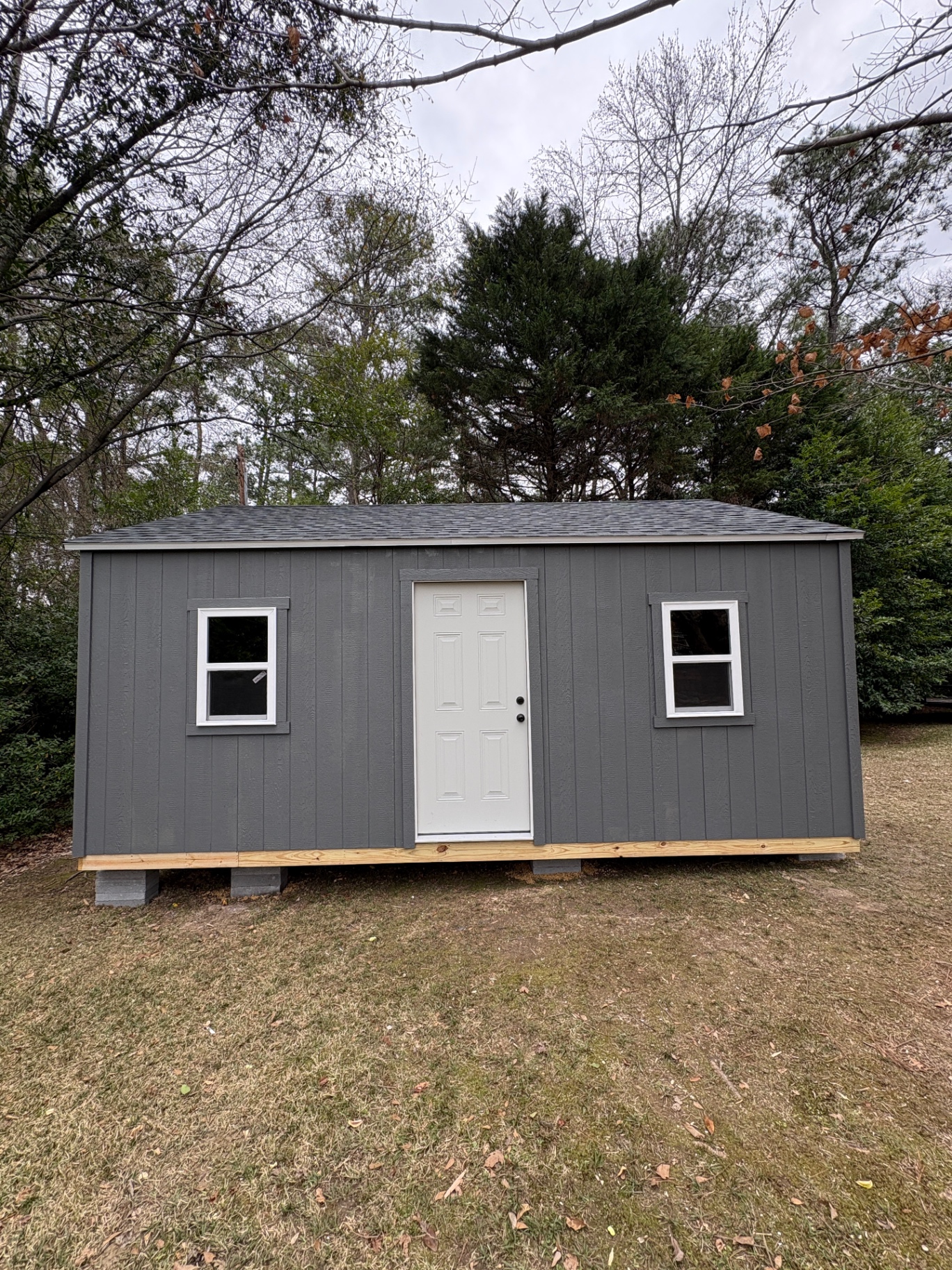 Charcoal shed with a white six-panel house door centered on the long wall and a standard window on each side
