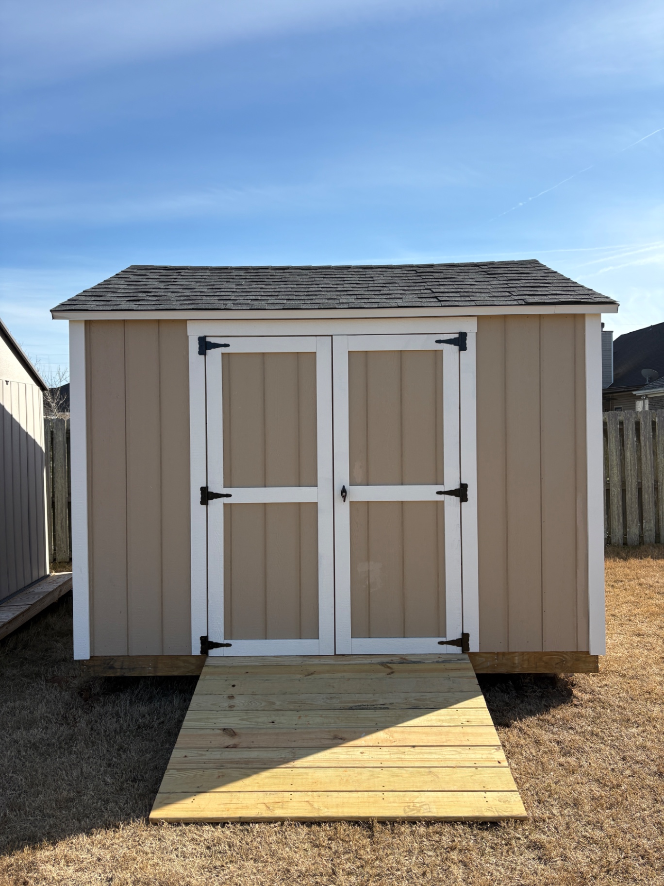 Tan shed with white-trimmed double doors and a treated wood ramp built to fit the doors