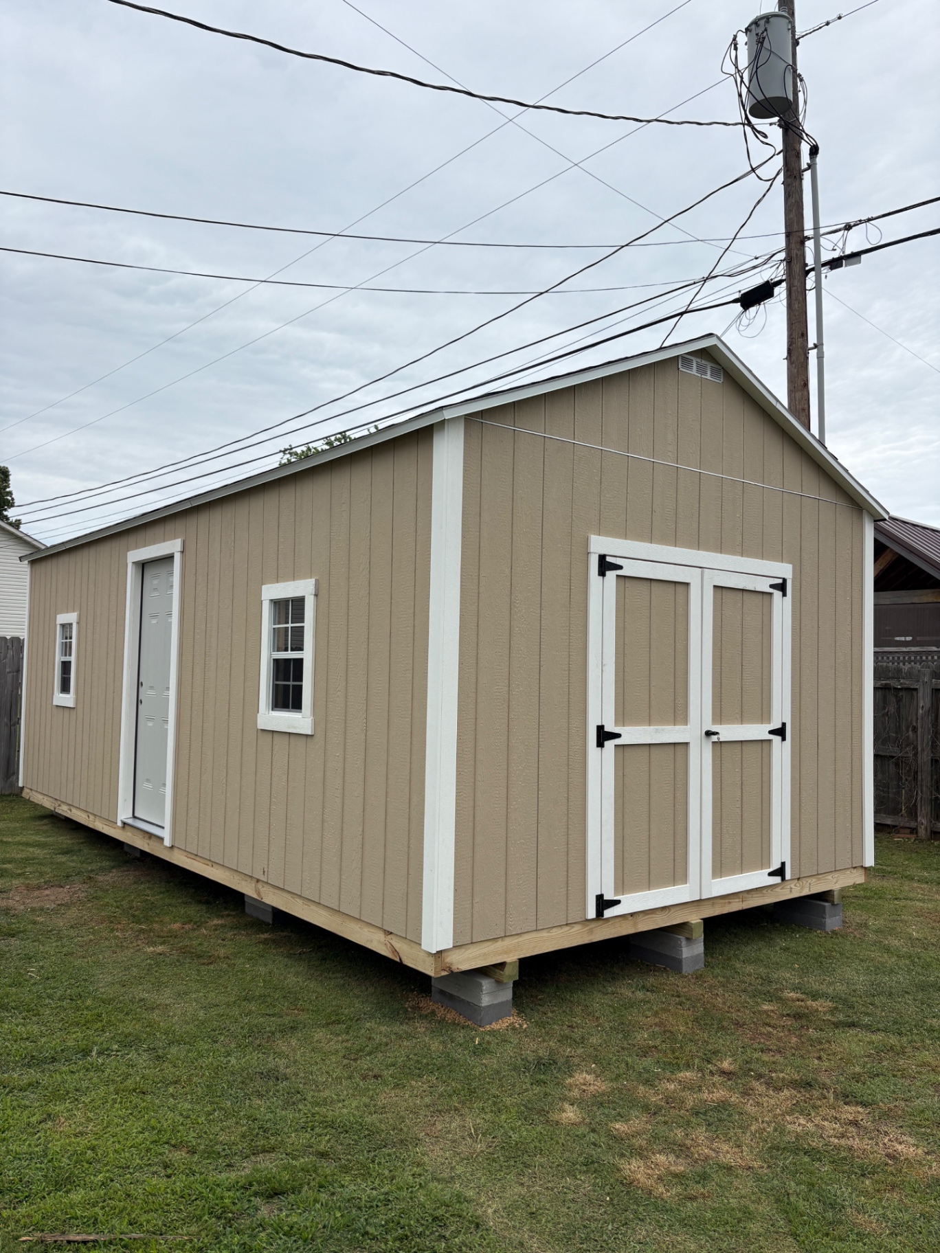 Long tan shed with a white house door and two windows on the side and white double doors on the gable end