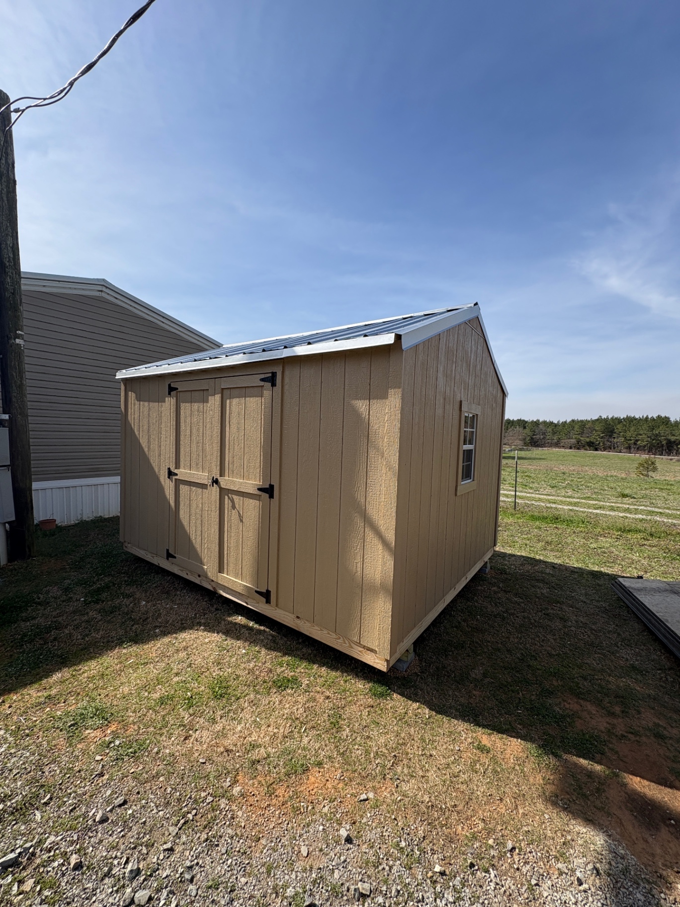 Angled view of a tan shed with matching double doors, a side window and a light-colored ribbed metal roof