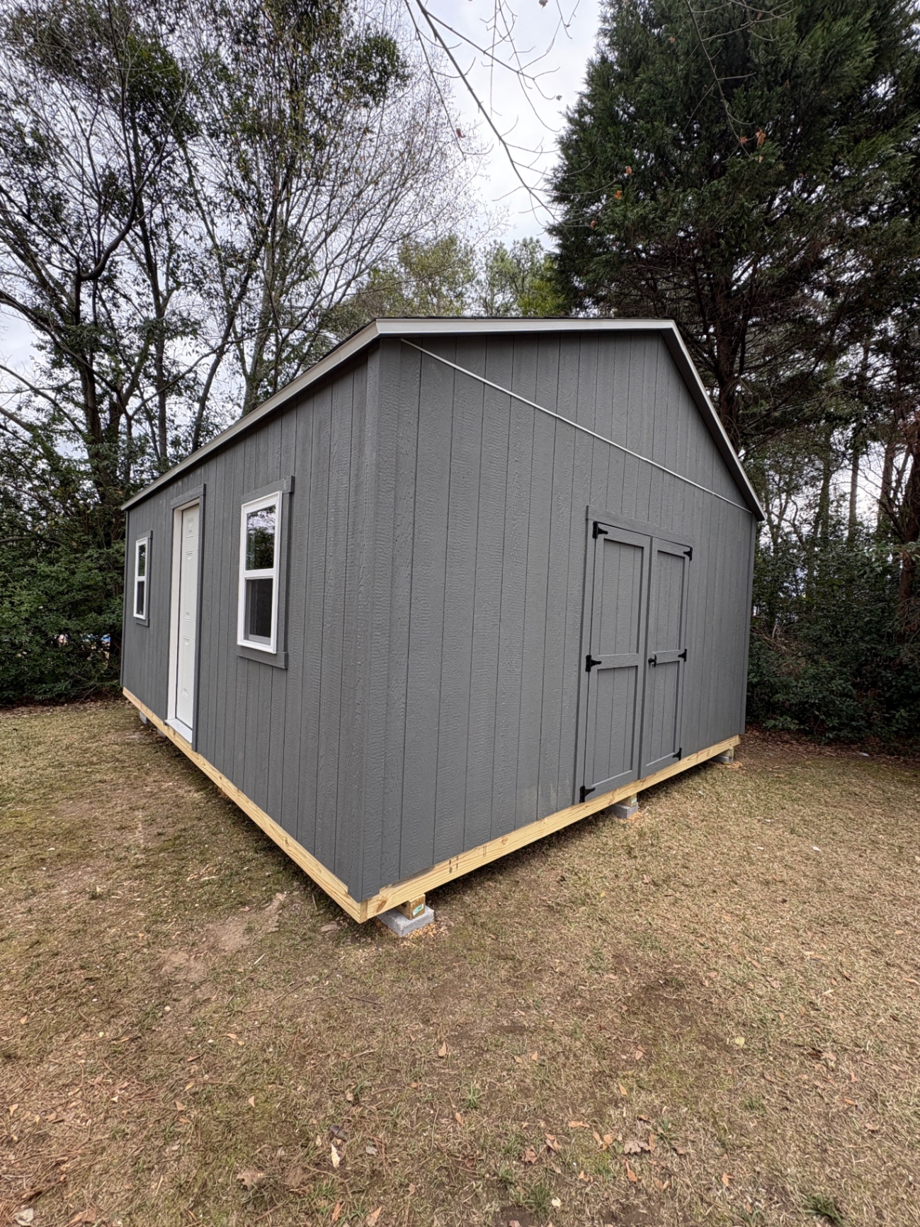 Corner view of a charcoal shed with double doors on the gable end and a house door with windows on the long wall