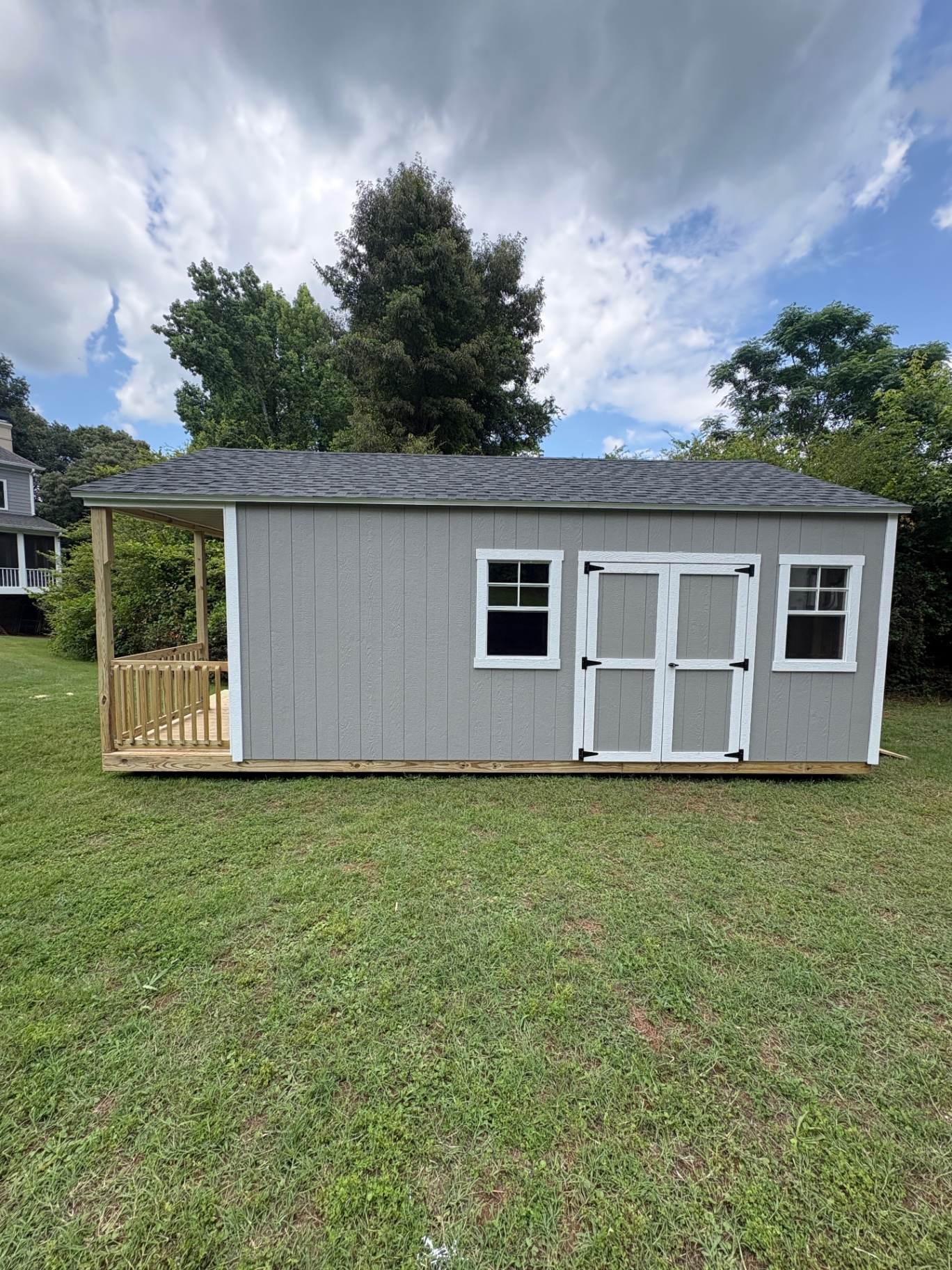 Gray shed with a covered porch on the left end, white double doors centered on the long side, and a window on each side