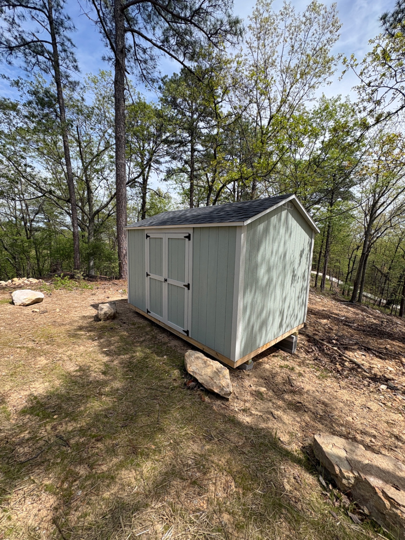 Angled view of a light seafoam shed with white-trimmed double doors on a wooded ridge