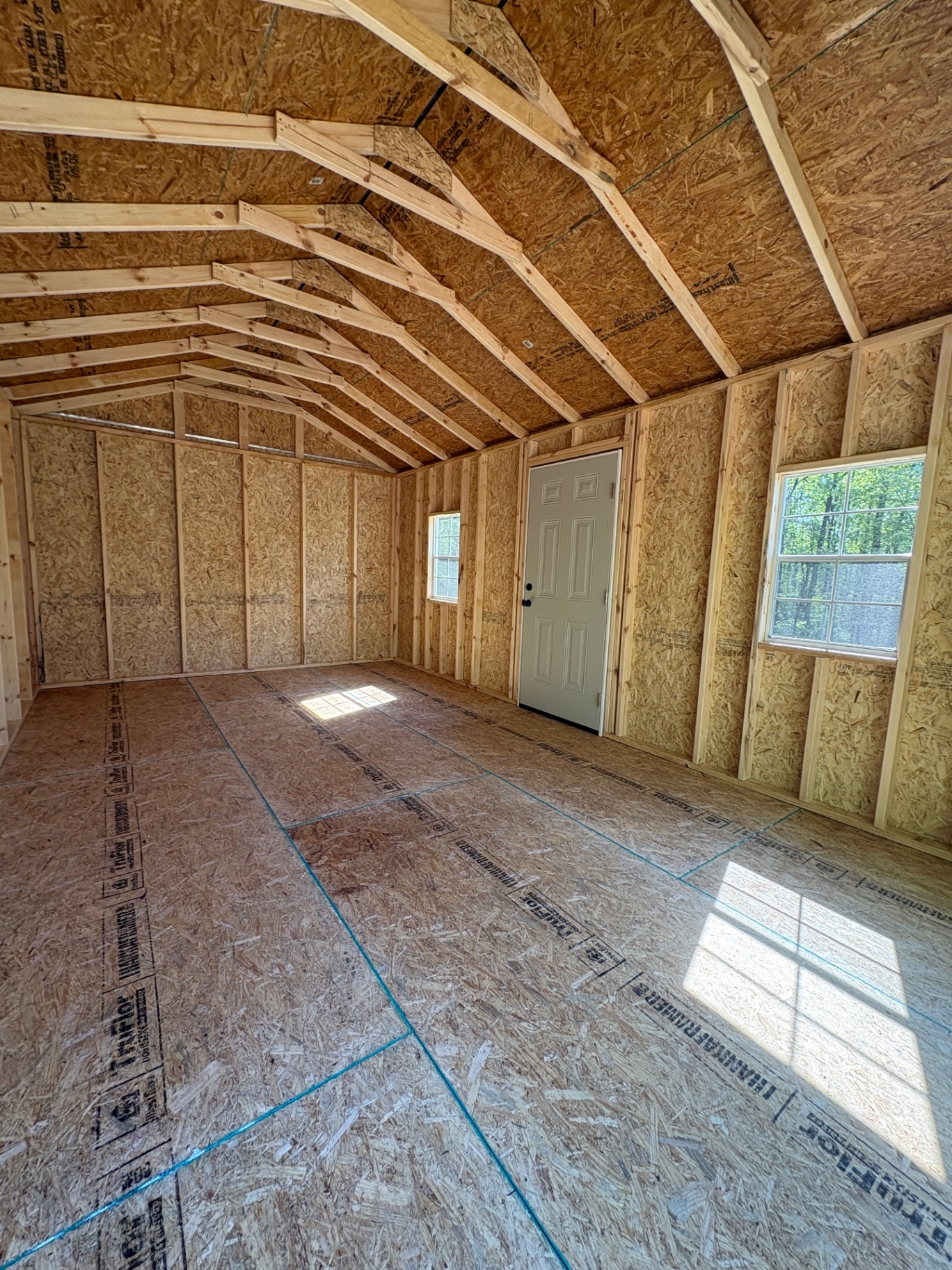 Shed interior with open rafters, a house door, two windows and a tongue-and-groove floor