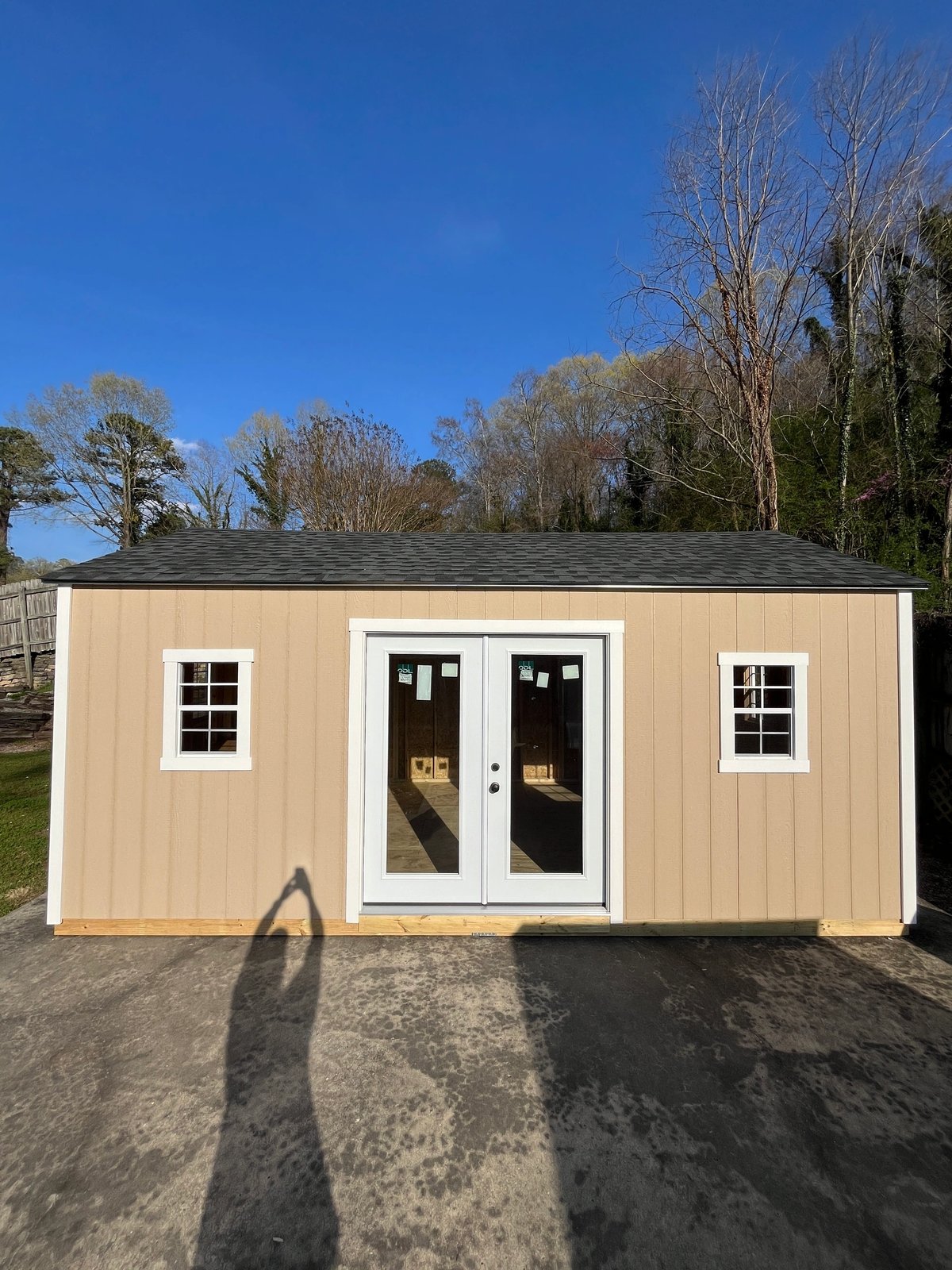 Tan shed with white French doors and a standard window on each side, built on a concrete driveway