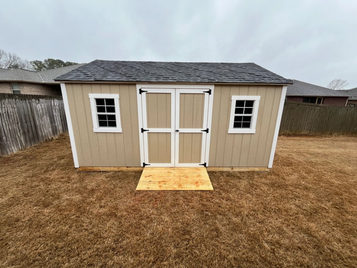 Long tan shed with white double doors, a standard window on each side and a treated wood ramp