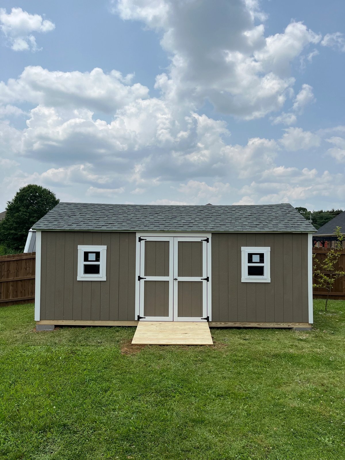 Mushroom gray shed with white double doors, a standard window on each side and a treated wood ramp