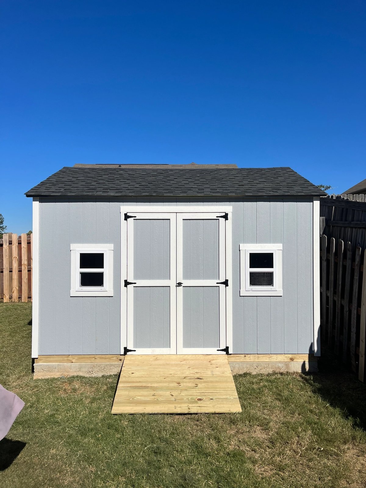 Light gray shed with white double doors, a standard window on each side and a treated wood ramp