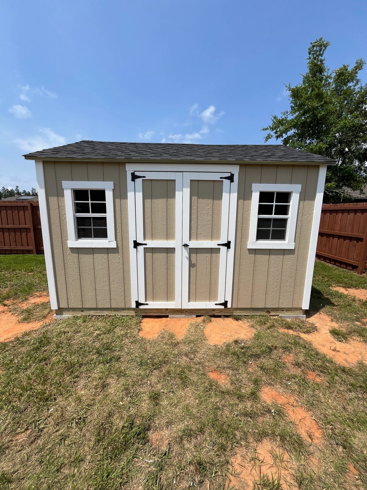Tan shed with white double doors and a standard window on each side, built on treated runners