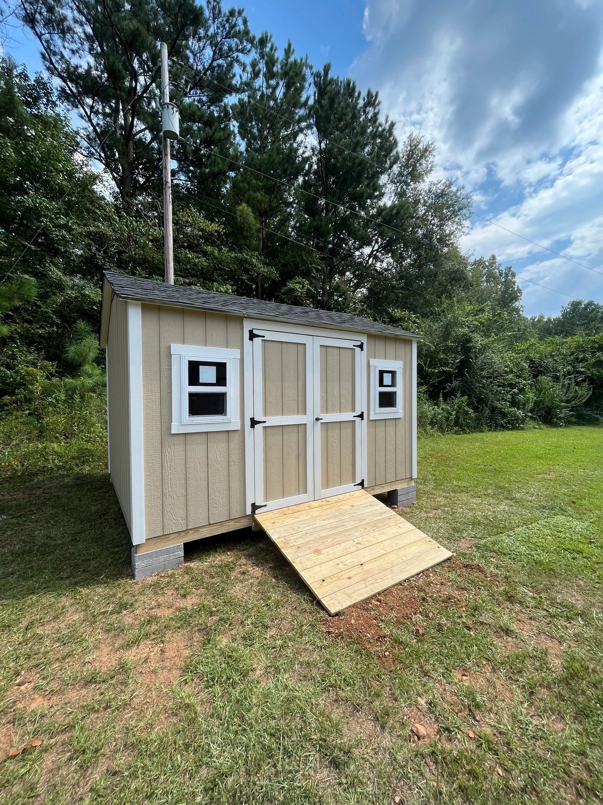 Tan shed with white double doors, two standard windows and a treated wood ramp