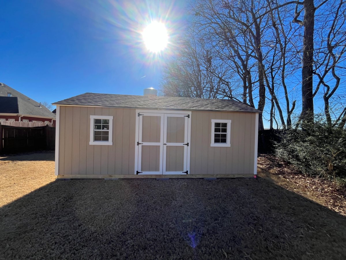 Tan shed with white double doors and a standard window on each side, sun directly behind it