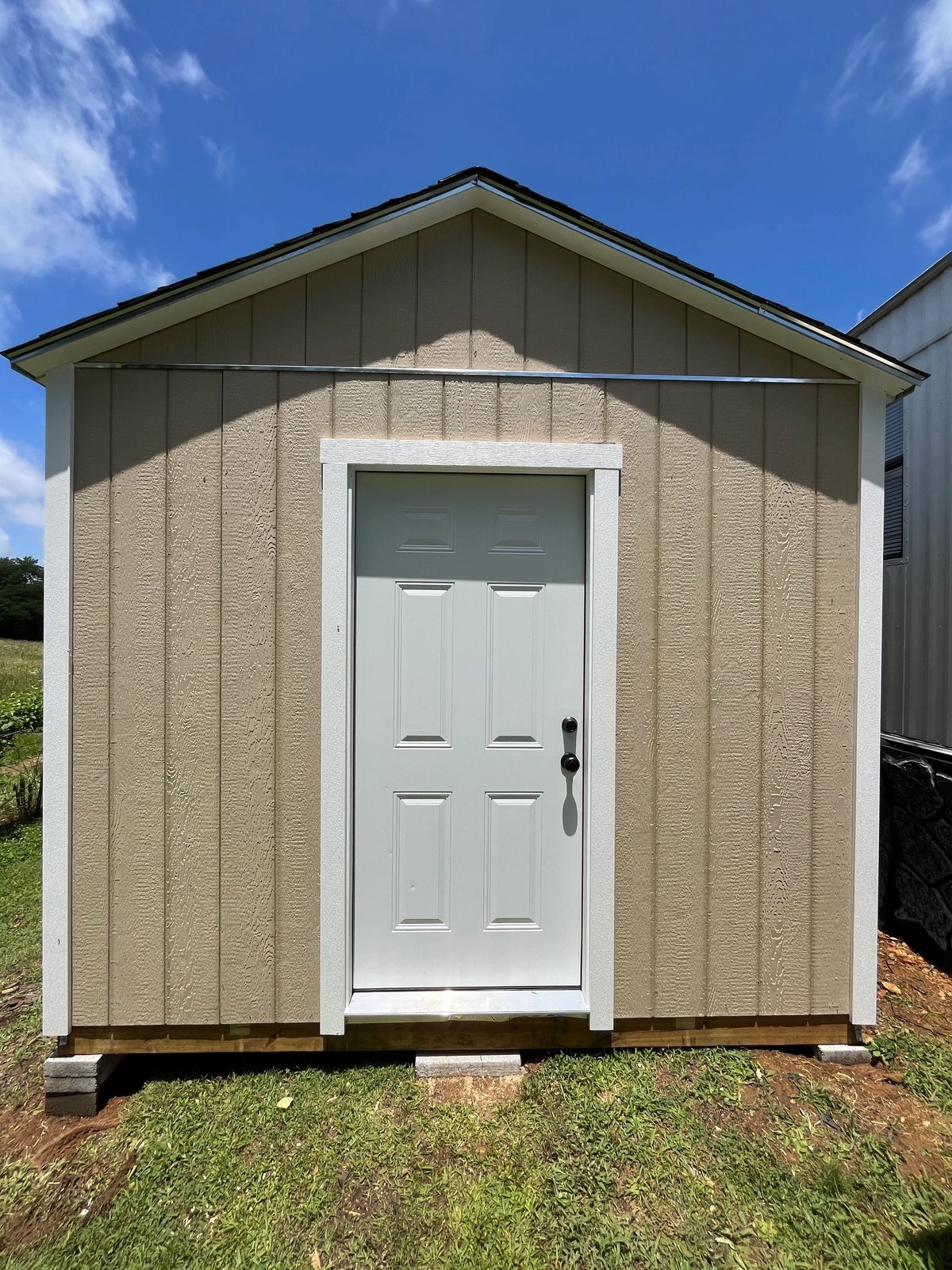 Tan shed with a white six-panel house door centered on the gable end