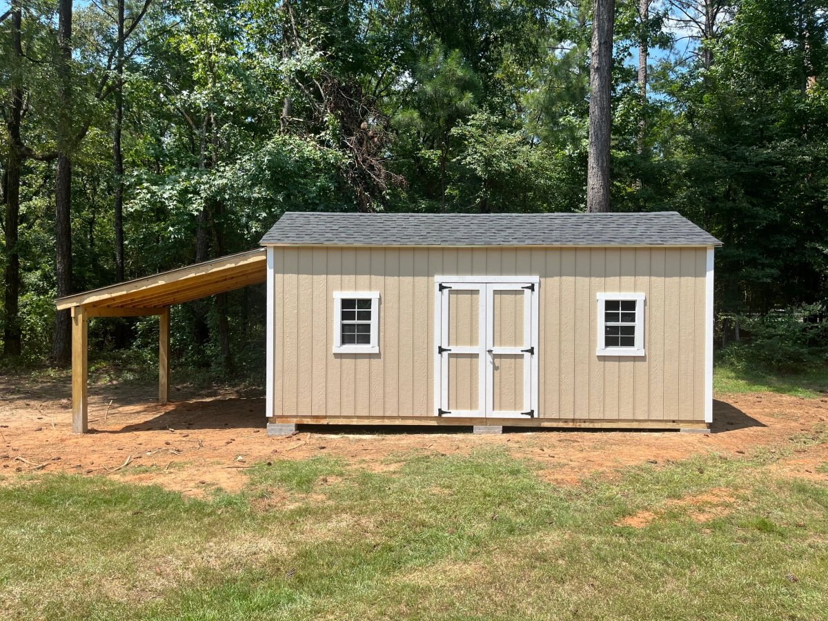 Tan shed with white double doors and two standard windows, with an open lean-to roof extending off one end